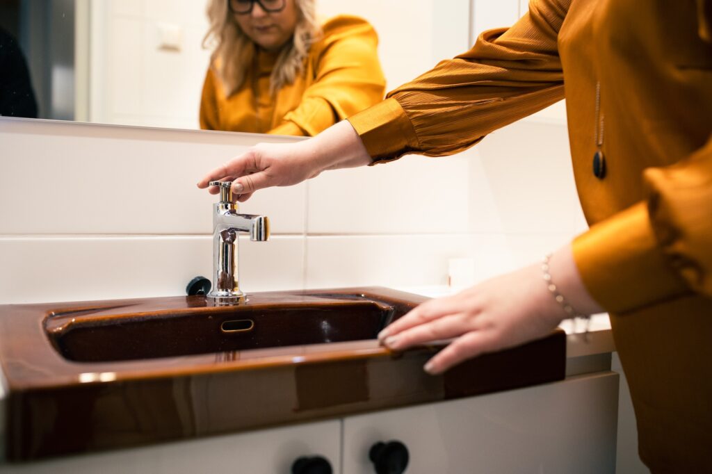 Kuvassa nainen on avaamassa wc:n vesihanaa.